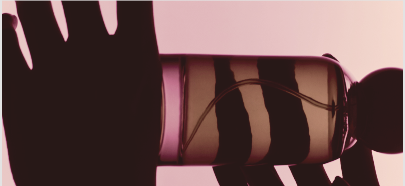 Hand holding a striped beauty oil bottle against a pink background